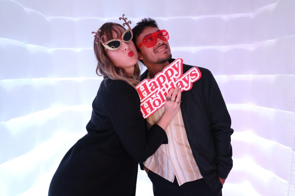 Couple wearing funny sunglasses and holding a holiday photo booth prop
