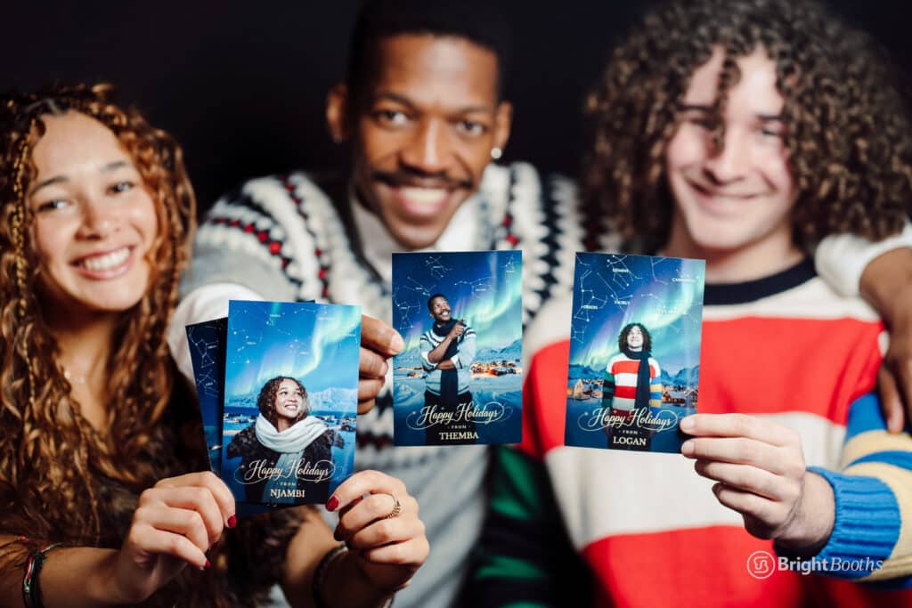 Group of friends holding Holiday Constellation photo booth prints with personalized messages and northern lights